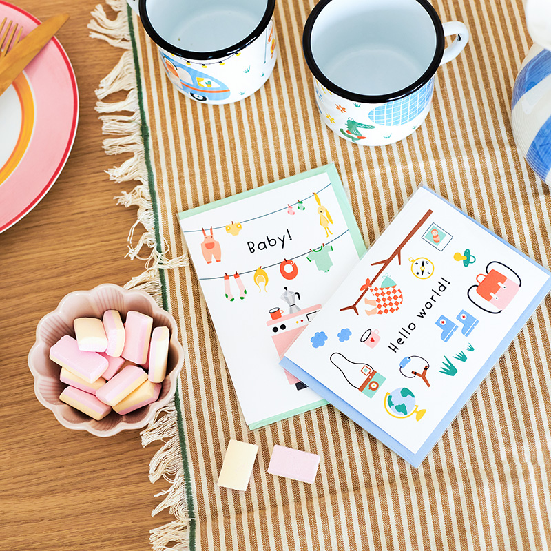 Grappige wenskaart voor een pasgeboren baby met de tekst: Hello World. De kaart toont een baby in een knapzak, omringd door avontuurlijke items zoals een kompas, laarzen, katapult, rugzak etc. Perfect voor de avontuurlijke ouders.