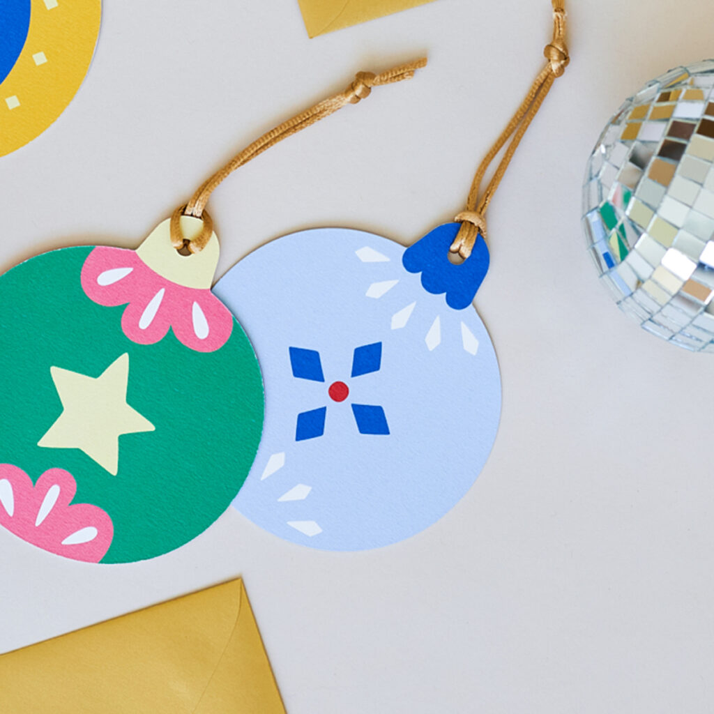 Vrolijke kerstbal kaart met een schitterende sneeuwster in koele blauwe tinten, aangevuld met een sprankje rood. Gemaakt van stevig 510 grams papier, perfect als ornament, cadeau of kaart voor de feestdagen.