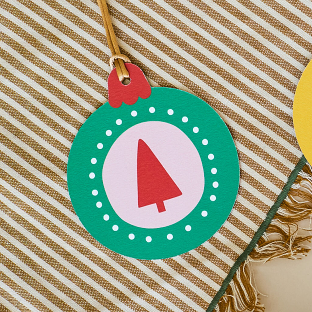 Stevige papieren kerstbal met kerstboomillustratie, duurzaam en kleurrijk. Perfect voor de feestdagen, dubbelzijdig bedrukt en geleverd met kaart en envelop. Unieke kerstdecoratie en feestelijke wenskaart in één.