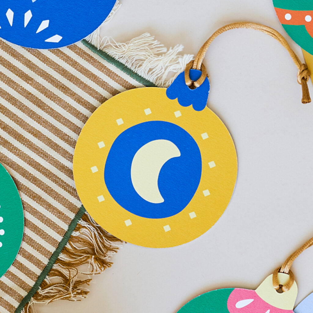 Stevige papieren kerstbal met een heldere en vrolijke illustratie van een maan. Gemaakt van duurzaam materiaal, ideaal voor een milieuvriendelijke kerstversiering. De kerstbal heeft een levendige uitstraling, perfect voor in de kerstboom of als kleurrijke decoratie.